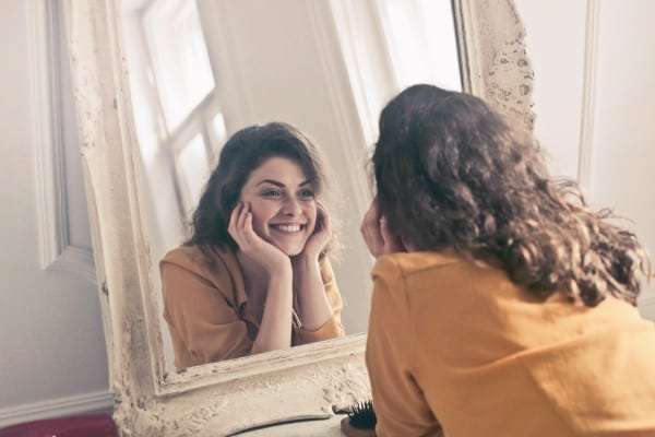 Frau schaut in den Spiegel und ist glücklich wegen ihres Erfolgjournals